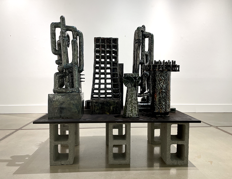 Black ceramic sculpture on top of wood balanced on cinderblocks in art gallery 
