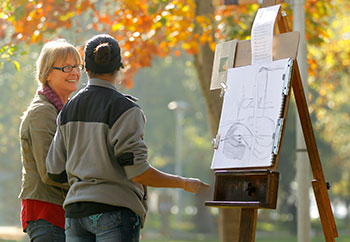 Faculty talks to student artists working outdoors amid fall colors.