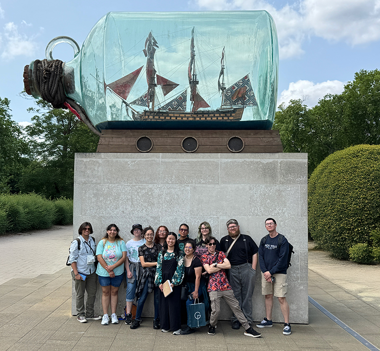 a group of people standingin front of a large ship in a bottle sculpture outside