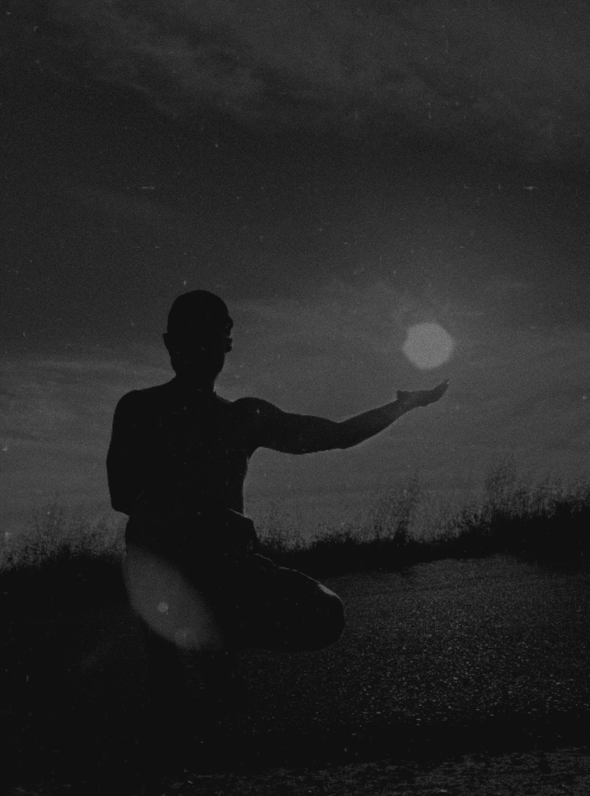 Black and white photo of a person holding their hand up to the sun. 