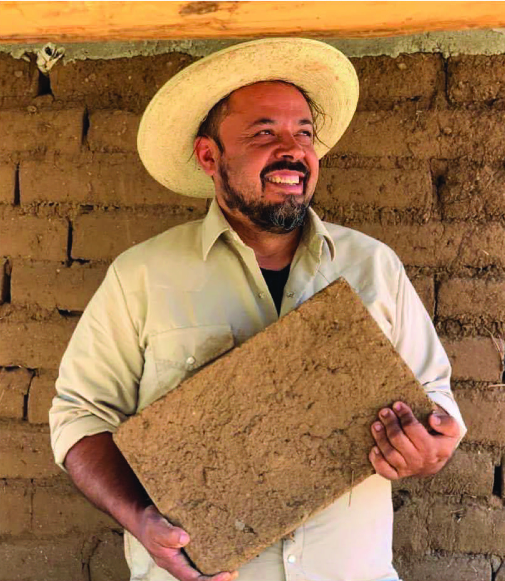 Hispanic Man in tan shirt and hat holding a large adobe brick