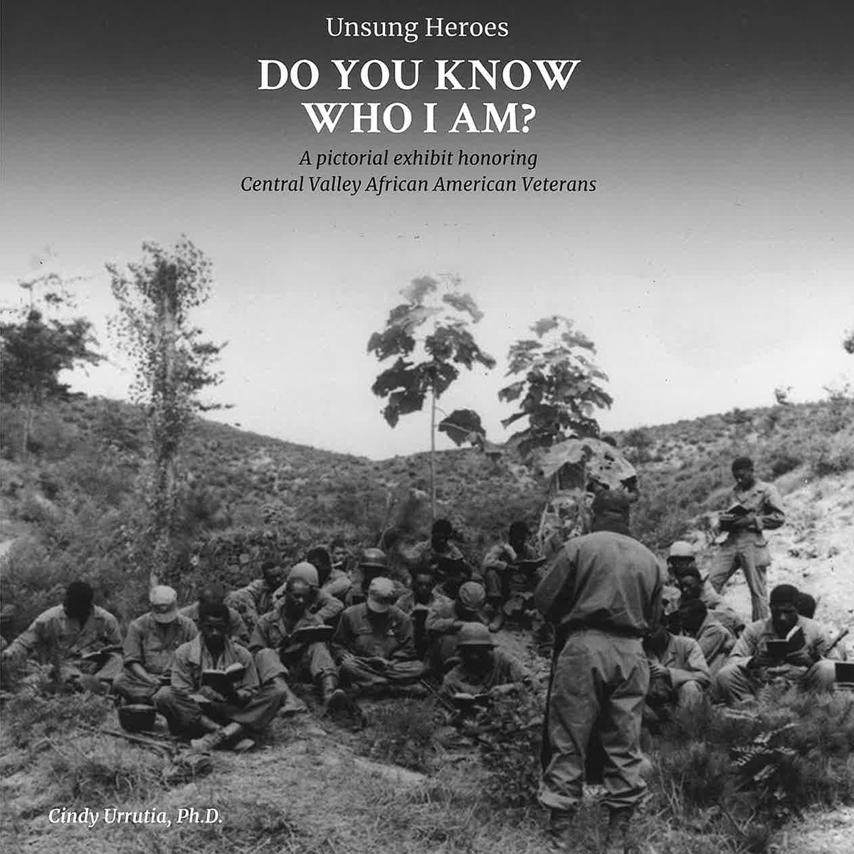 Black and white photo of Black soldiers in the huddled in the field reading books.