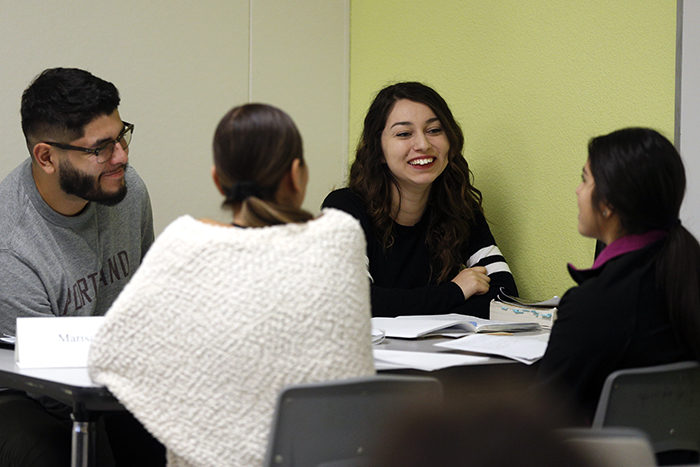 Four smiling students sit around a workshop table together inside the Writing Center.