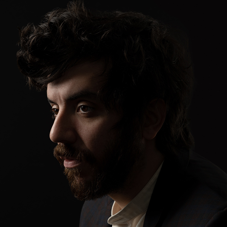 Headshot of Kaveh in profile, wearing a white shirt and dark jacket.