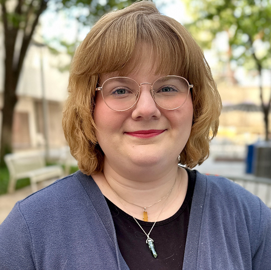Headshot of Victoria with courtyard and greenery in background.