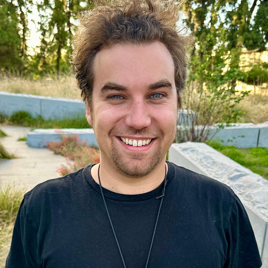 Headshot of Nicholas, with greenery in background.