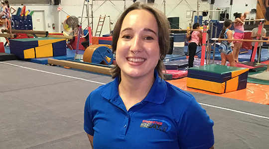 Headshot of Samantha Golden with a busy gymnastics gym in background.