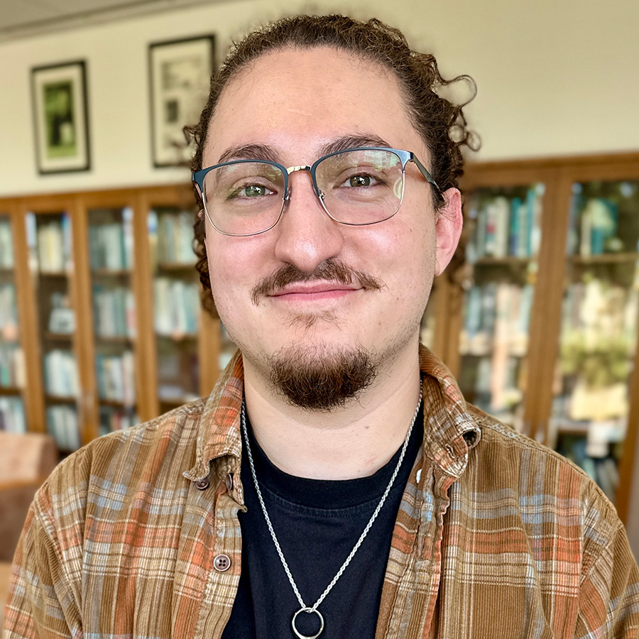 Headshot of Peter with bookshelves in background.