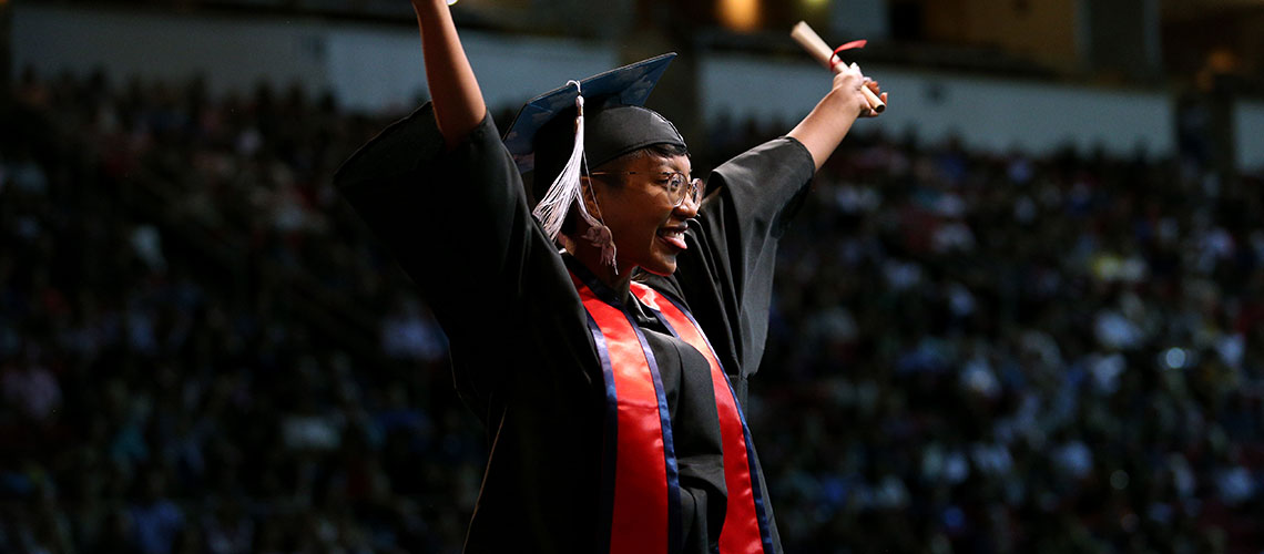 College of Arts and Humanities grad waves to crowd with diploma in hand