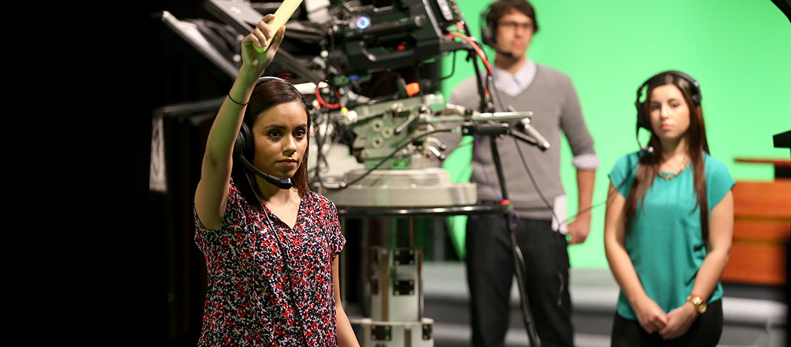 Student television newscast director raises her hand as cameras prepare to roll on set.