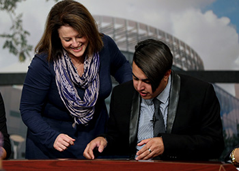 A professor helps a student at the desk in the campus television studio.