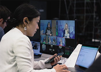 A professor works at a computer in a television control room.