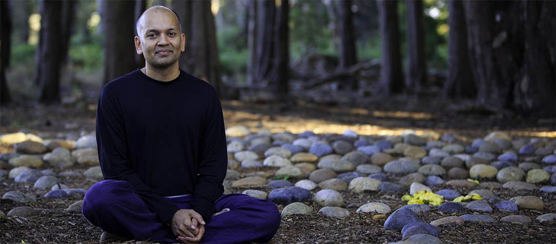 Nipun Mehta sitting in front of the tress cross legged